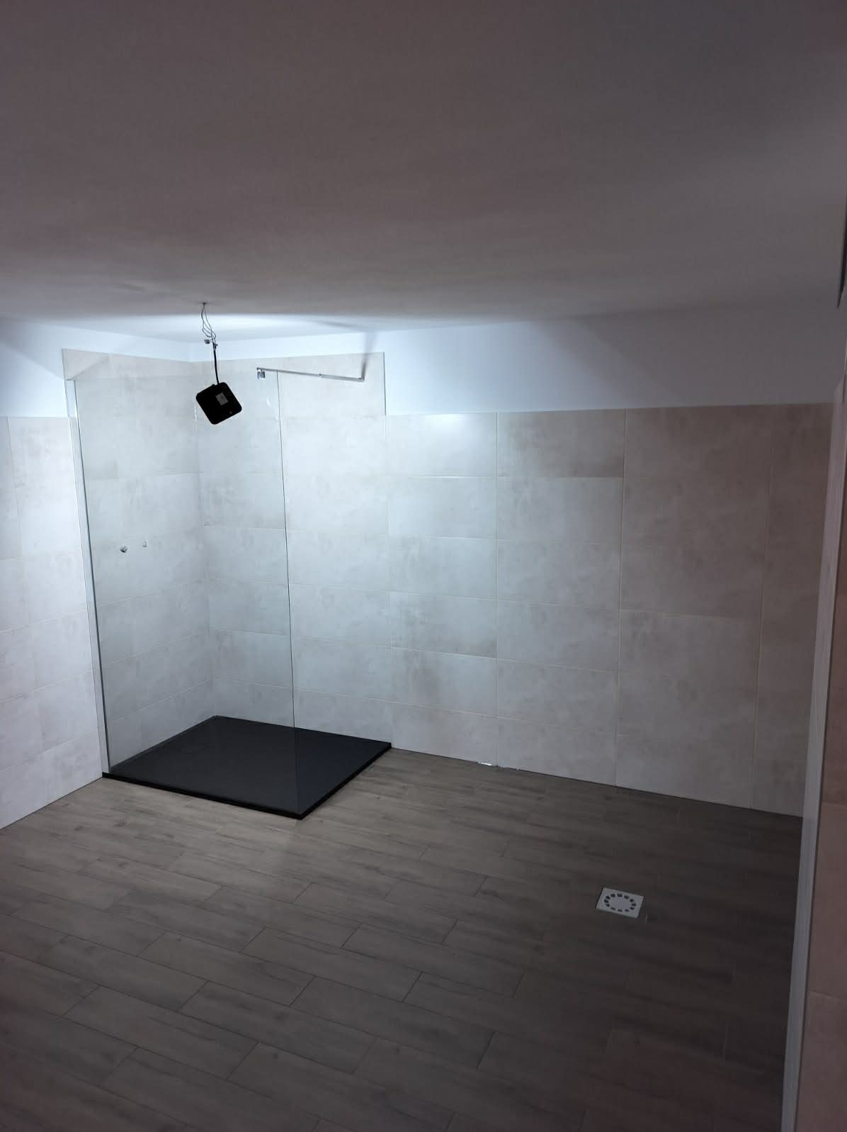 Nowoczesna łazienka z kabiną prysznicową typu walk-in, wykończona płytkami w odcieniach beżu i szarości. Widoczny czarny brodzik i drewnopodobna podłoga.