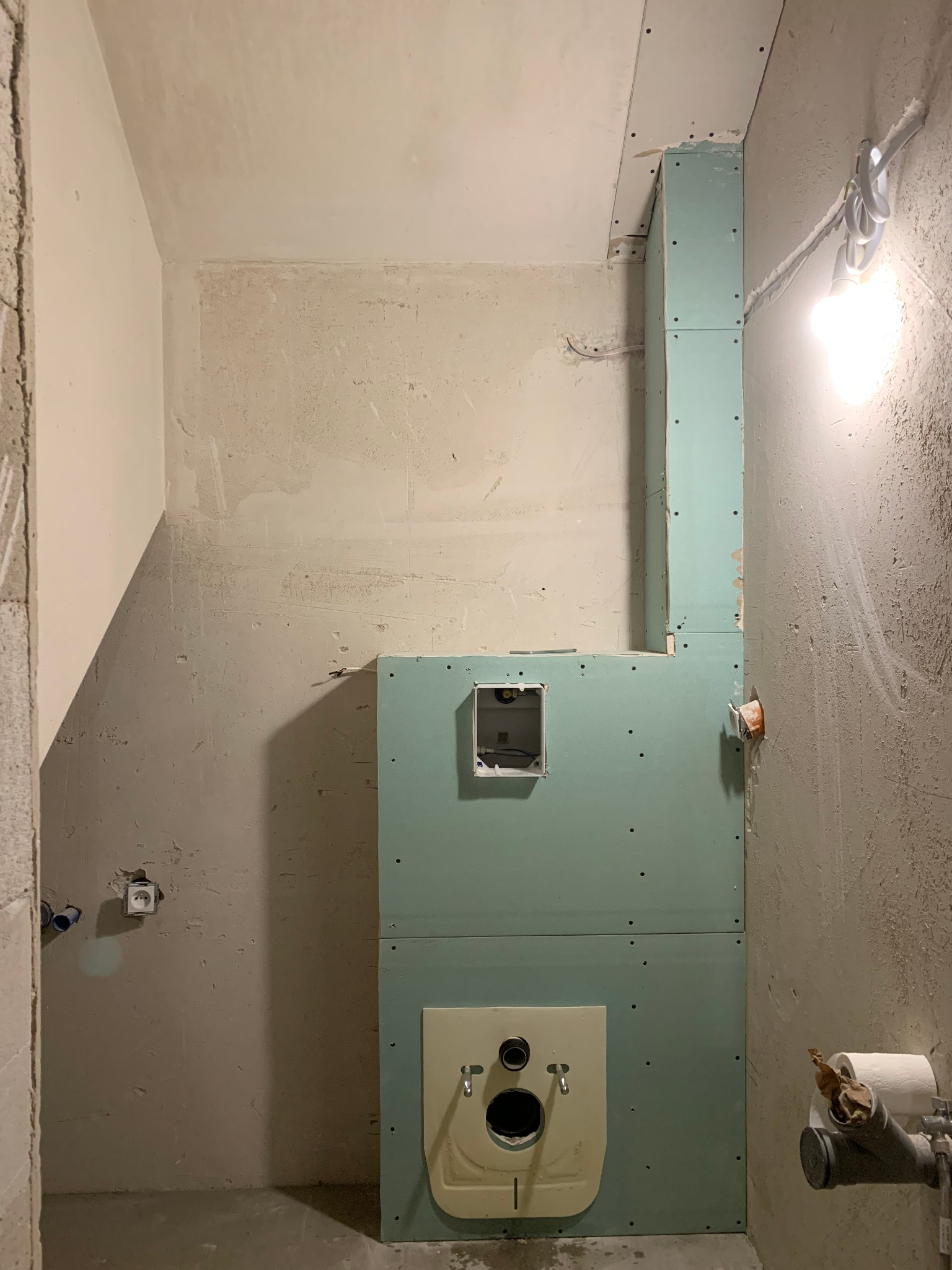 Montaż stelaża podtynkowego WC z płyt karton-gips na nierównej ścianie w trakcie remontu łazienki. Widoczne instalacje i surowy stan wykończenia.