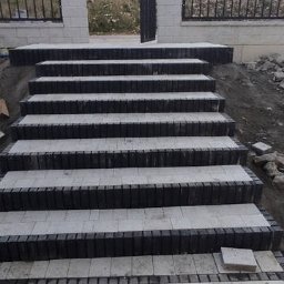 Greks-Bud - Schody z kostki brukowej prowadzące do furtki w Ujsołach. Stopnie wykończone ciemną obwódką, całość w odcieniach szarości. Widok na zewnątrz posesji.