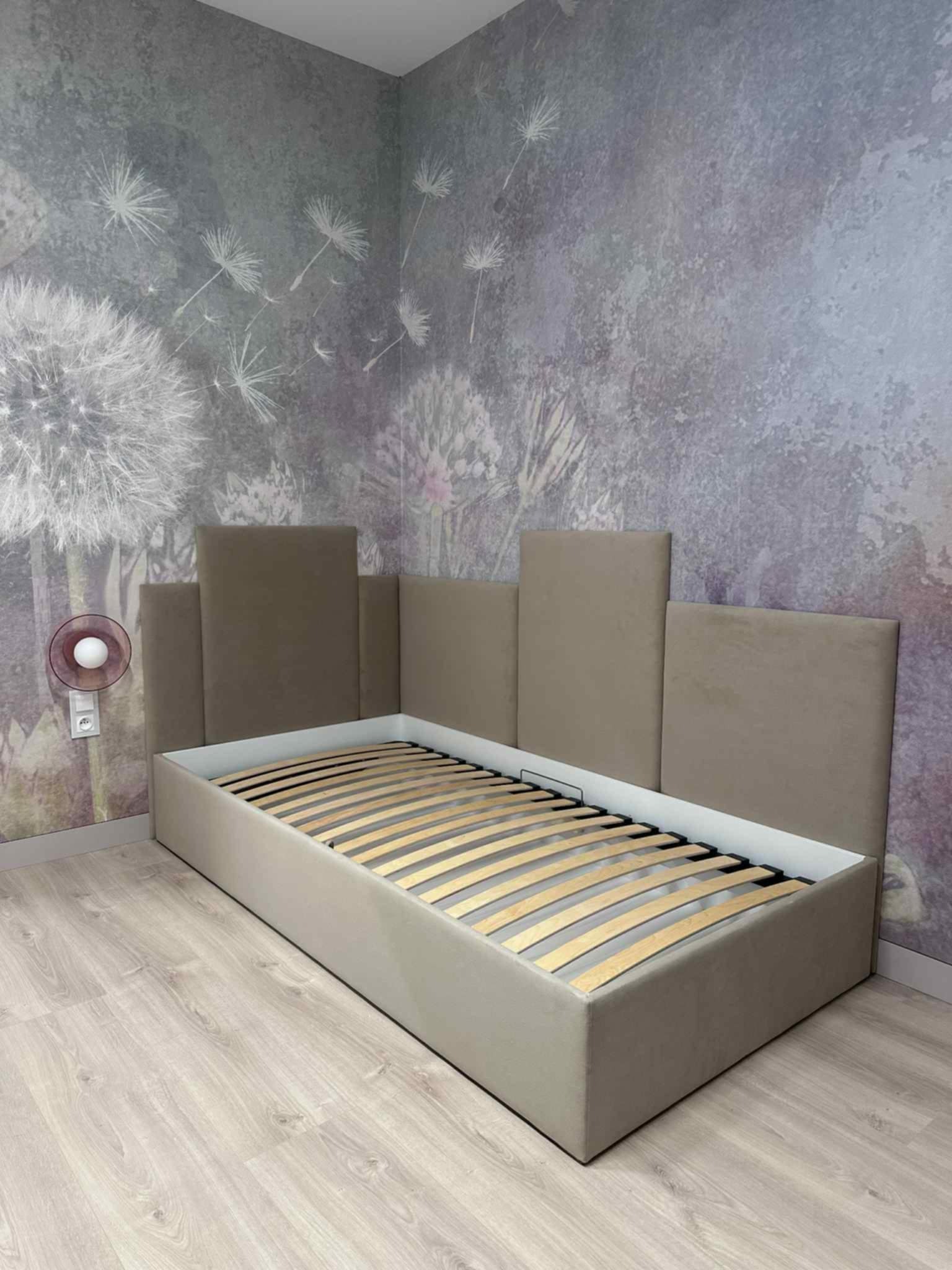 Tapicerowane łóżko jednoosobowe z wezgłowiem w odcieniach beżu, z drewnianym stelażem, na tle ściany z motywem dmuchawców i lampką nocną.