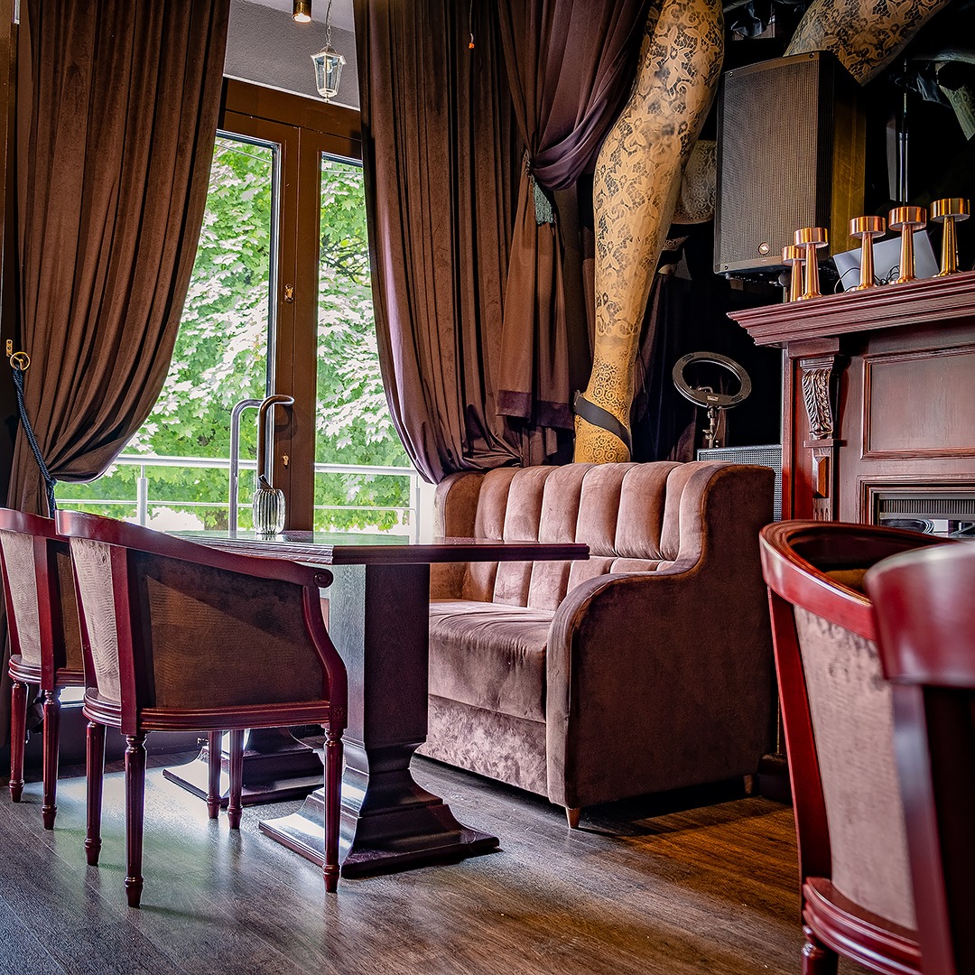 Stylowa, tapicerowana sofa w odcieniach brązu, z krzesłami i stolikiem w eleganckim wnętrzu w Turośni Kościelnej. Dekoracyjne zasłony i nietypowe ozdoby.