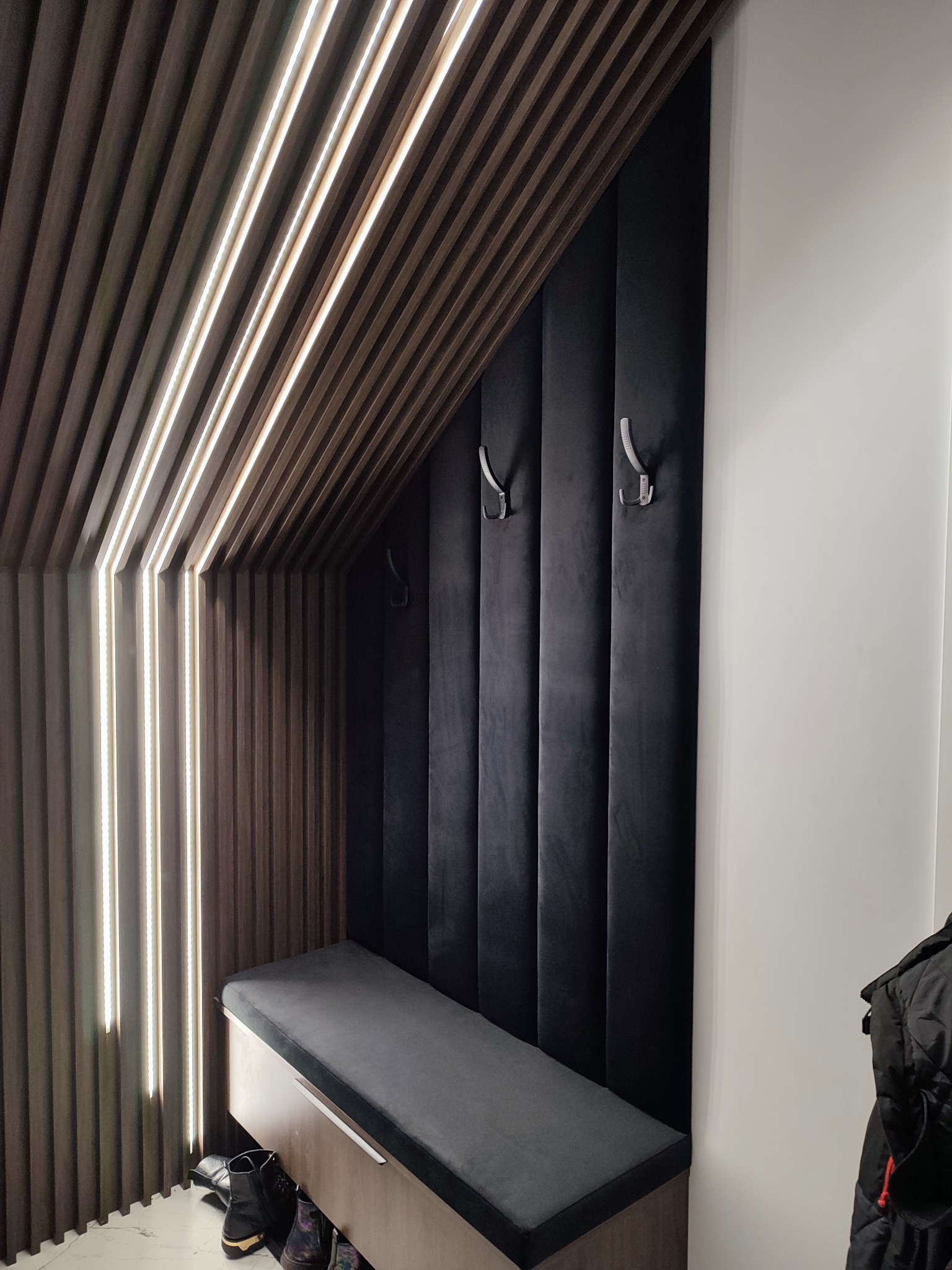 Tapicerowany panel ścienny w kolorze grafitu z wieszakami i siedziskiem, drewniane lamele z oświetleniem LED, nowoczesny design przedpokoju.