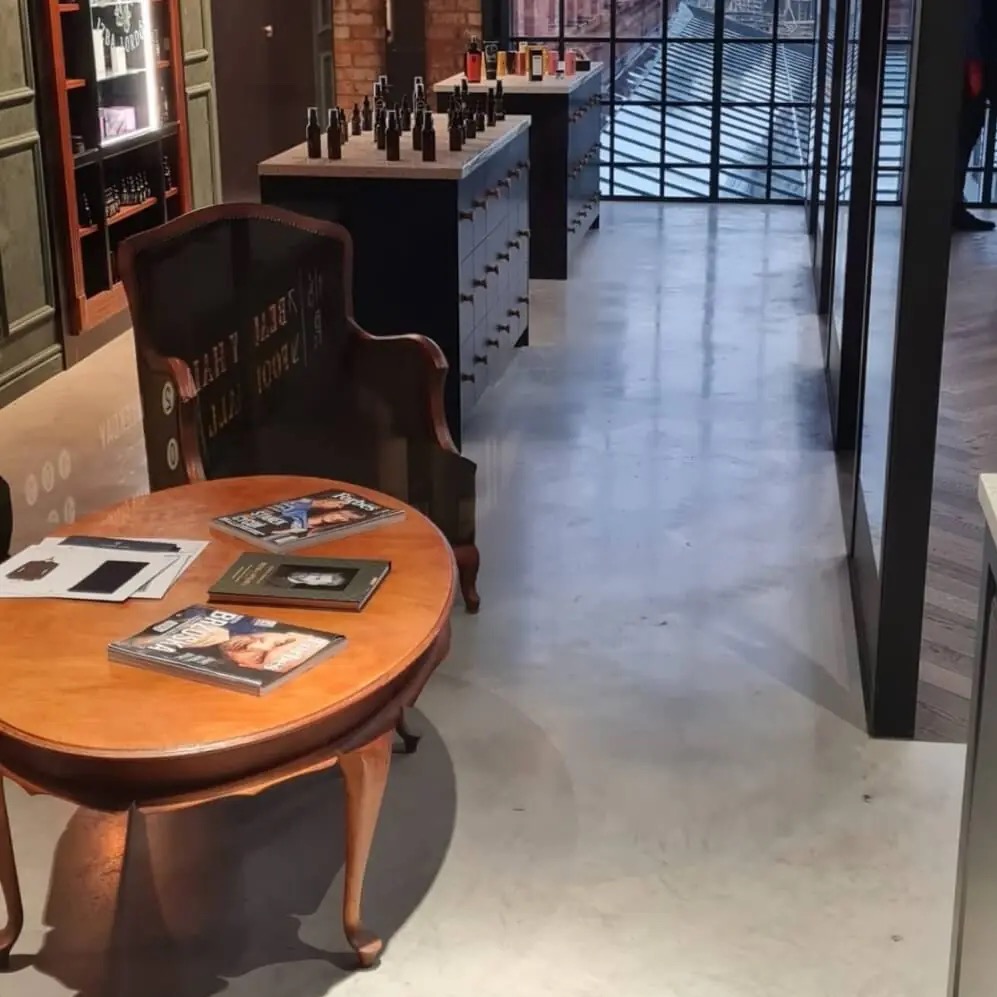 Jasnoszara posadzka żywiczna w nowoczesnym salonie z drewnianym stolikiem i krzesłem. W tle ekspozycja produktów na czarnych wyspach.