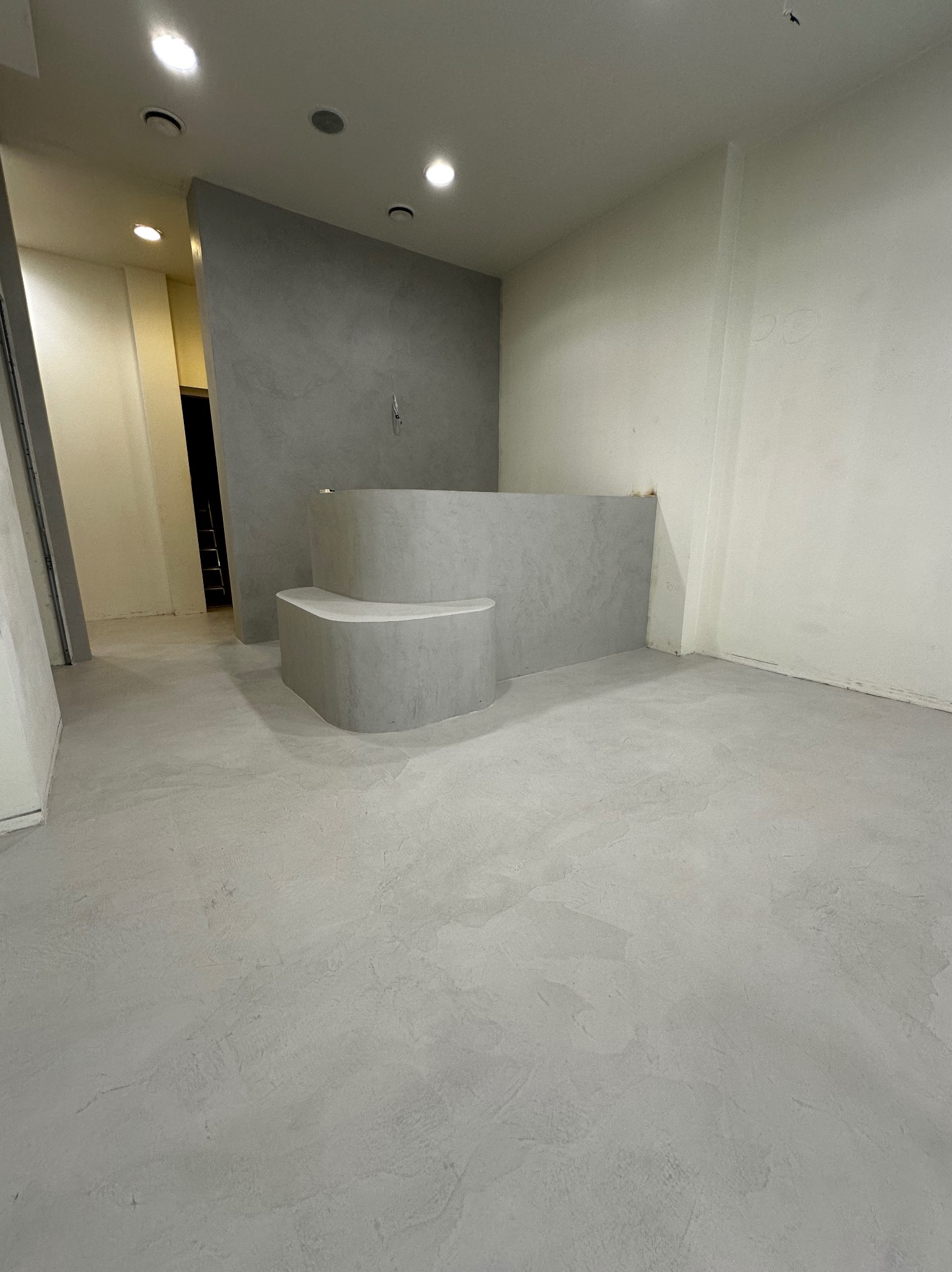 Minimalistyczne wnętrze po wykończeniu: szara posadzka z mikrocementu, ściany w odcieniach szarości i bieli, z elementami dekoracyjnymi w formie stopni.