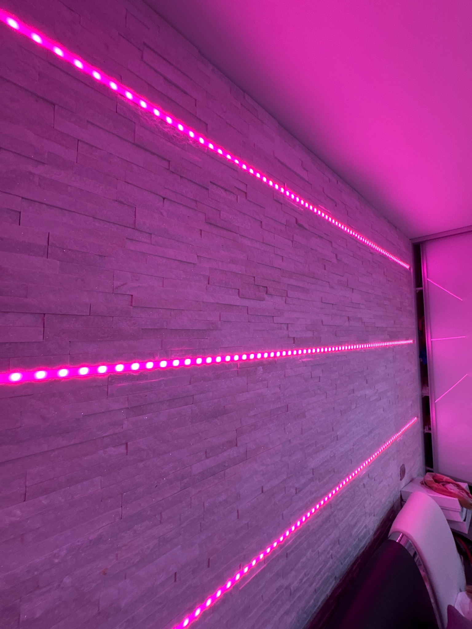 Ściana z dekoracyjną, podświetlaną listwą LED w odcieniach różu, tworząca nowoczesny akcent w pomieszczeniu. Widoczna faktura kamienia na ścianie.