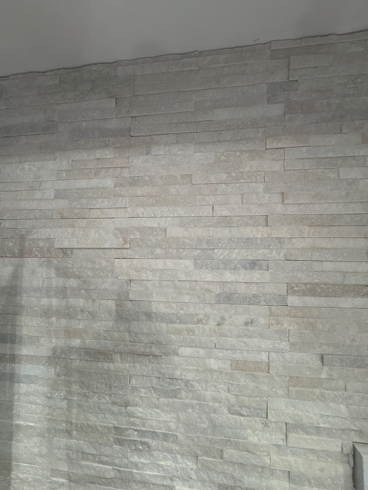 Ściana wykończona dekoracyjną, szarą okładziną z wąskich, poziomych płytek imitujących kamień. Widoczne subtelne różnice w odcieniach i fakturze poszczególnych elementów.