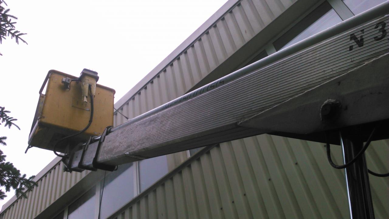 Żółty kosz podnośnika na tle szarej ściany budynku. Widoczny fragment wysięgnika z numerem 'N 3'.