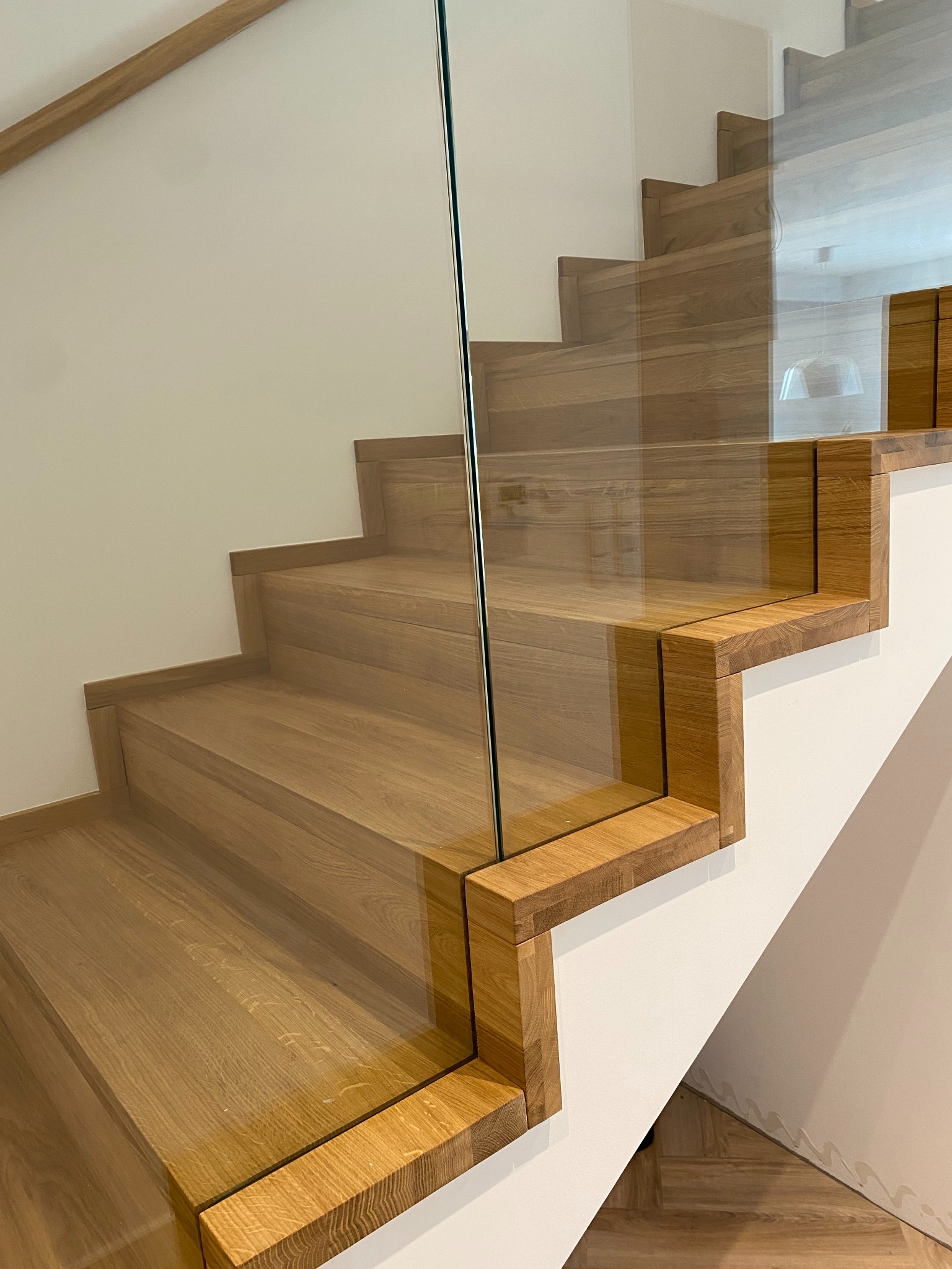 Nowoczesne schody z drewna dębowego z balustradą ze szkła hartowanego, widok z dołu, jasne wnętrze, minimalistyczny design.