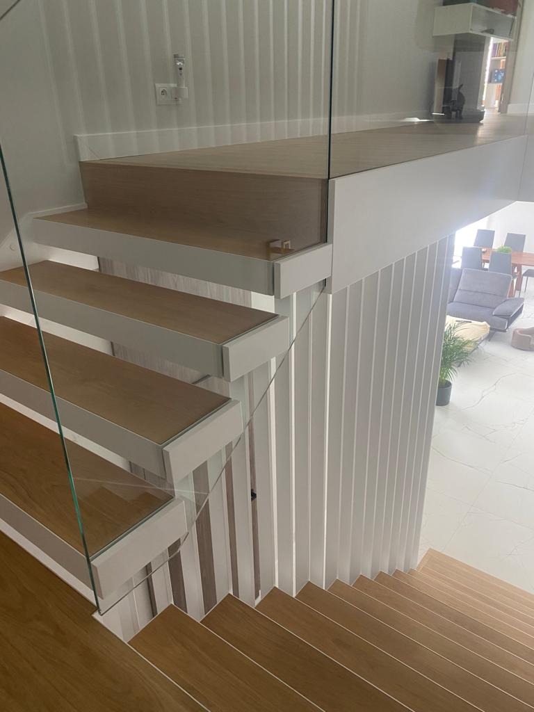 Nowoczesne schody z drewnianymi stopniami i szklaną balustradą, białe elementy wykończeniowe, widok z góry, jasne wnętrze.