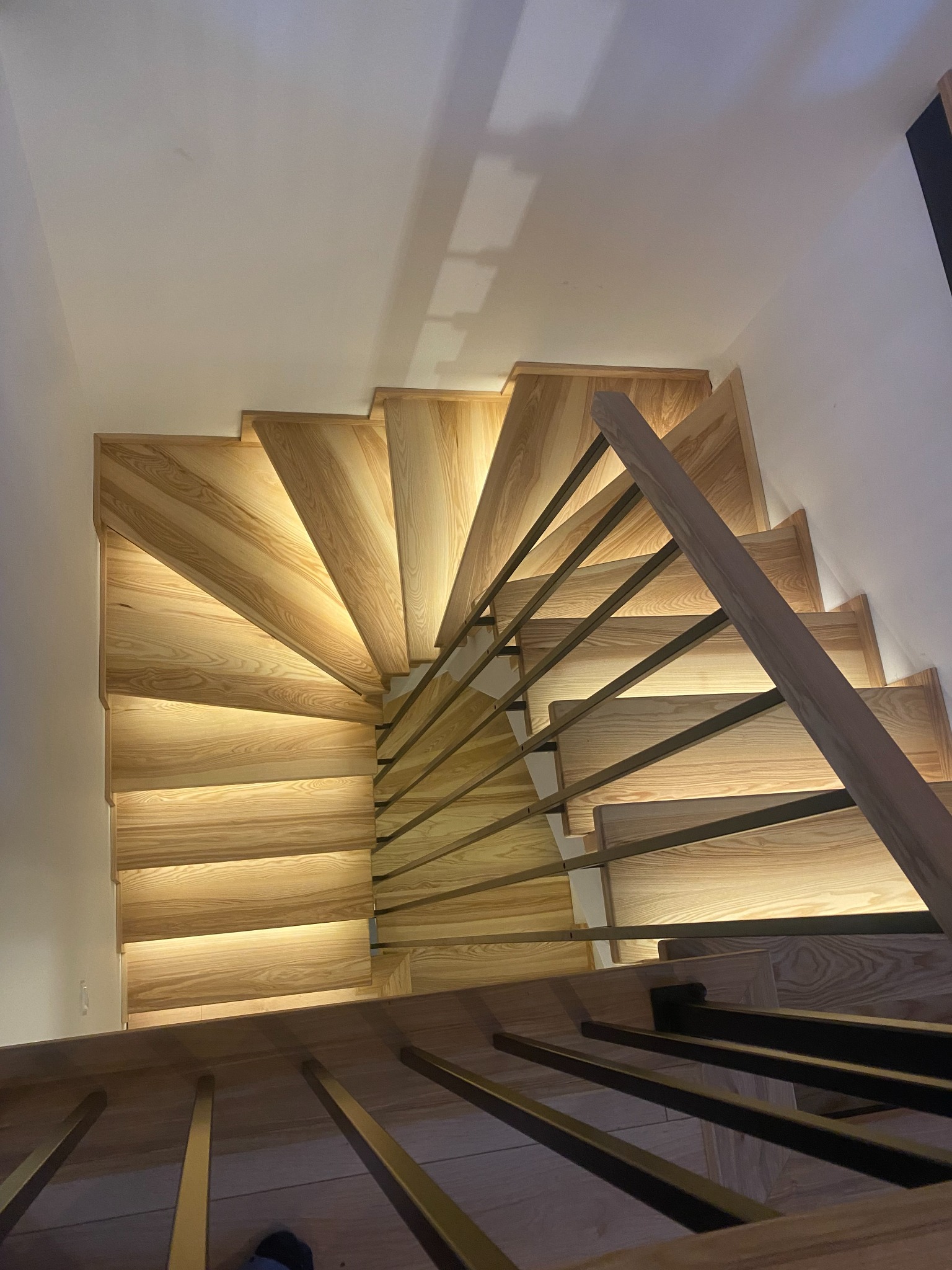 Spiralne schody z jasnego drewna z podświetleniem LED i metalową balustradą, widok z góry w Kąpinie. Nowoczesny design i precyzyjne wykonanie.