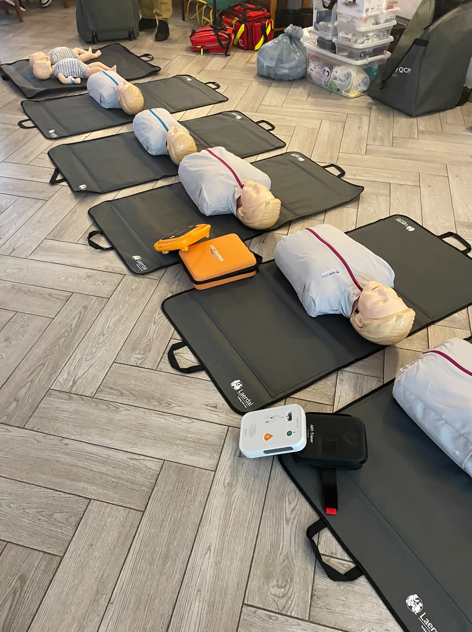 Sala szkoleniowa z manekinami do resuscytacji na matach Laerdal, AED Trainer i torbami medycznymi, przygotowana do kursu pierwszej pomocy.