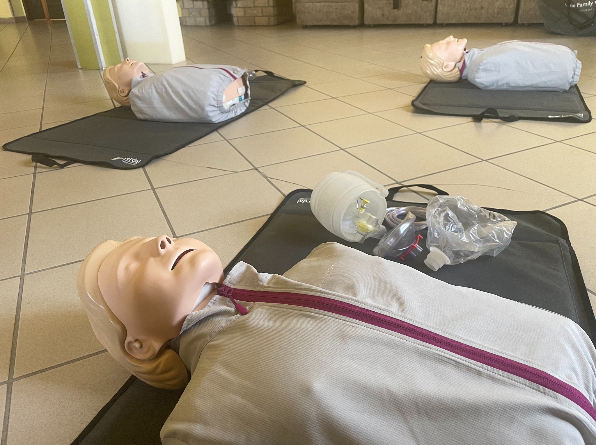 Manekiny do ćwiczeń RKO na matach, widoczne akcesoria do resuscytacji. Sala szkoleniowa z jasną podłogą. Przygotowanie do praktycznego szkolenia z pierwszej pomocy.