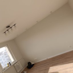 Maiki - Jasne, świeżo pomalowane wnętrze pokoju w Będkowie z drewnianą podłogą, widok na okno i grzejnik. Minimalistyczny wystrój, czyste ściany i sufit.