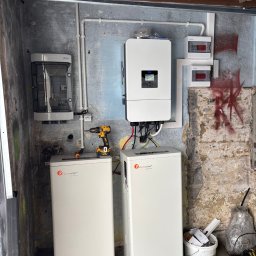 EcoConcept - Instalacja magazynu energii Felicity Solar z inwerterem na tle surowej ściany. Widoczne przewody, skrzynki elektryczne i narzędzia. Montaż w garażu lub pomieszczeniu gospodarczym.