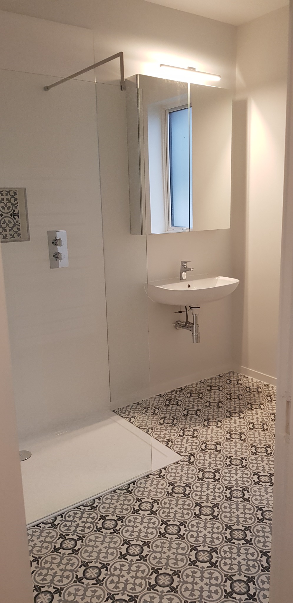 Nowoczesna łazienka z kabiną prysznicową typu walk-in, umywalką nablatową i wzorzystą podłogą w odcieniach szarości. Minimalistyczny design, jasne oświetlenie.