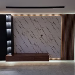 IPERFE - Nowoczesna ściana TV z marmurowym panelem, drewnianymi lamelami i czarną szafką z podświetlanymi półkami. Całość oświetlona listwami LED.