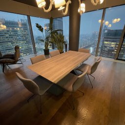 IPERFE - Nowoczesna jadalnia z drewnianym stołem i krzesłami na tle panoramy miasta za oknem. Designerska lampa sufitowa i drewniana podłoga dodają elegancji.