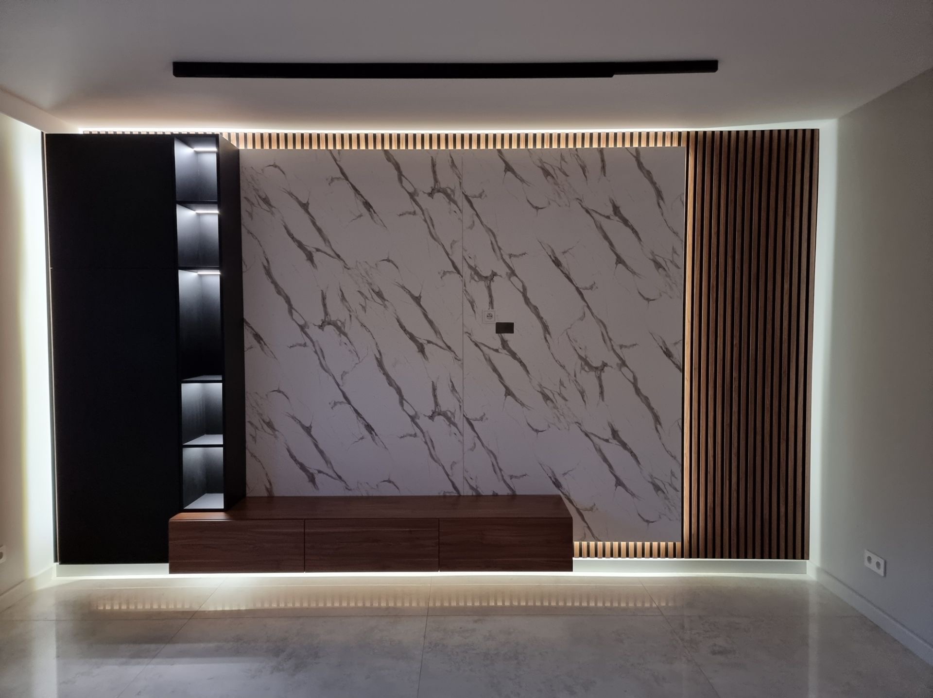 Nowoczesna ściana TV z marmurowym panelem, drewnianymi lamelami i czarną szafką z podświetlanymi półkami. Całość oświetlona listwami LED.