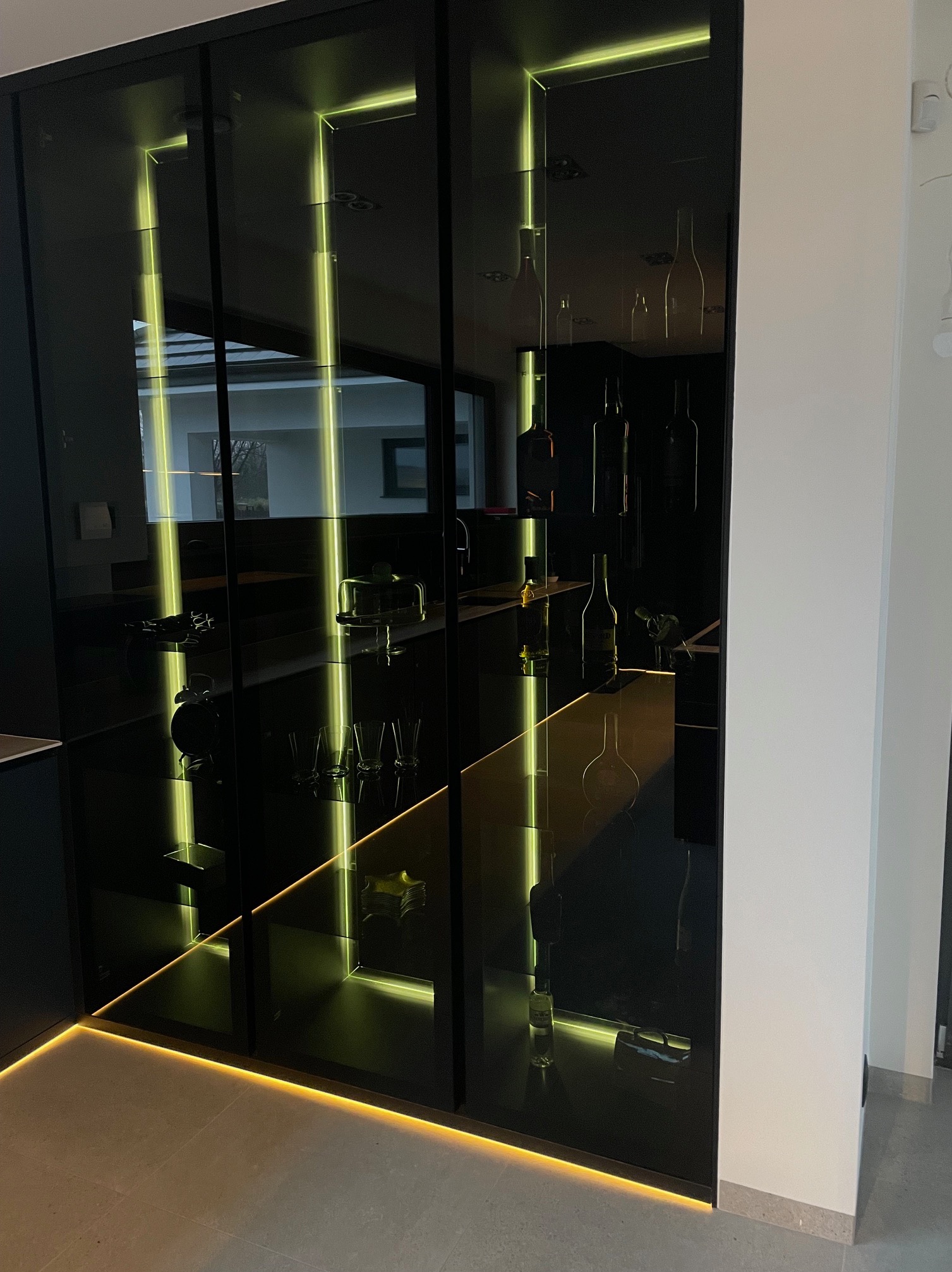 Nowoczesna, czarna szafa wnękowa z podświetleniem LED, eksponująca szkło, butelki i dekoracje. Minimalistyczny design, eleganckie wykończenie.