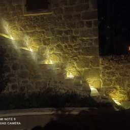 RM BAU Usługi Budowlane Robert Michalak - Kamienne schody zewnętrzne z oświetleniem punktowym wbudowanym w stopnie, nocne ujęcie z dołu, ciepłe światło podkreśla fakturę kamienia.