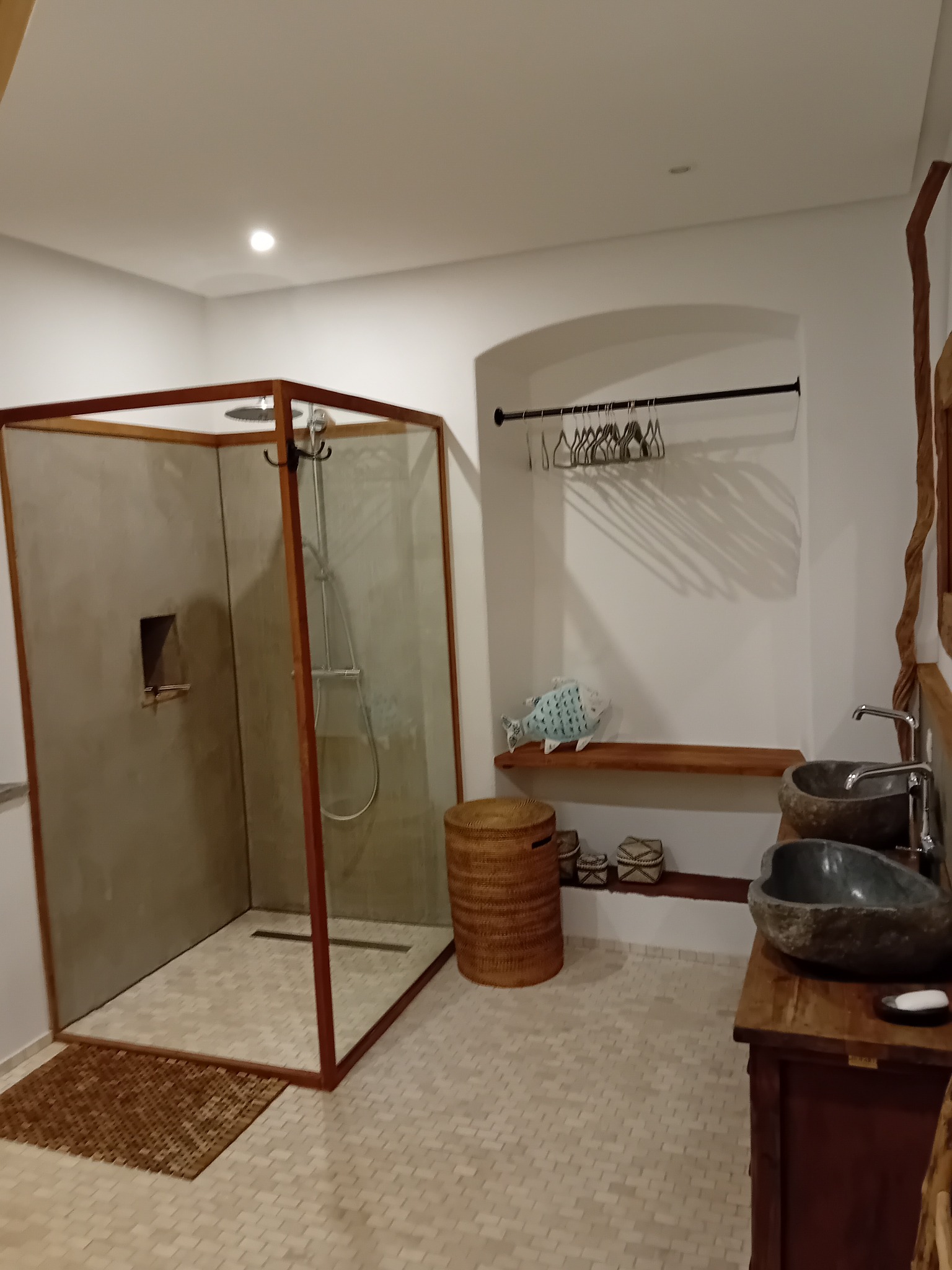 Nowoczesna łazienka z kabiną prysznicową typu walk-in, kamiennymi umywalkami i drewnianymi akcentami. Minimalistyczny design z naturalnymi materiałami.