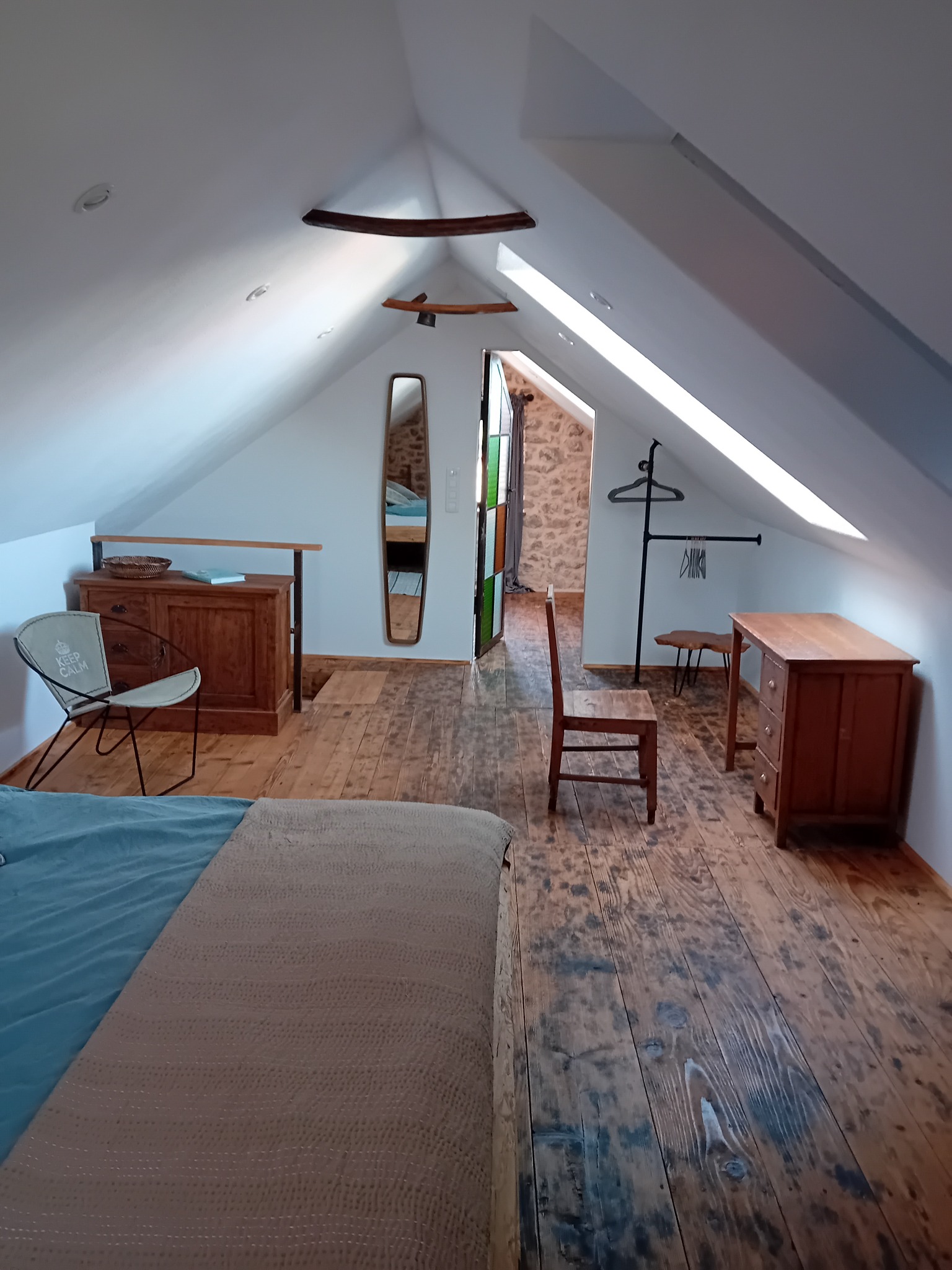 Stylowe poddasze z drewnianą podłogą i meblami w rustykalnym stylu. Widoczne skosy, okno dachowe i elementy dekoracyjne. Ustawne i przytulne wnętrze.