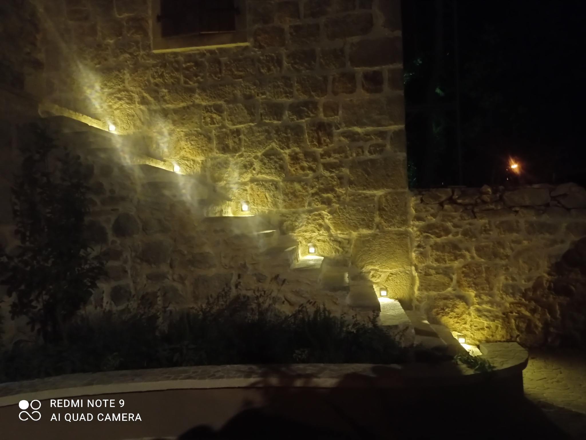 Kamienne schody zewnętrzne z oświetleniem punktowym wbudowanym w stopnie, nocne ujęcie z dołu, ciepłe światło podkreśla fakturę kamienia.