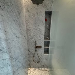 A.P. Kompleks - Nowoczesna kabina prysznicowa z marmurowymi ścianami, deszczownicą i wnęką z półkami. Minimalistyczny design, szklana ściana, odpływ liniowy. Eleganckie wykończenie łazienki.