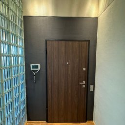 A.P. Kompleks - Nowoczesny przedpokój z ścianą z luksferów, drewnianymi panelami na suficie i ciemną ścianą z drewnianymi drzwiami. Podłoga wyłożona płytkami imitującymi drewno.
