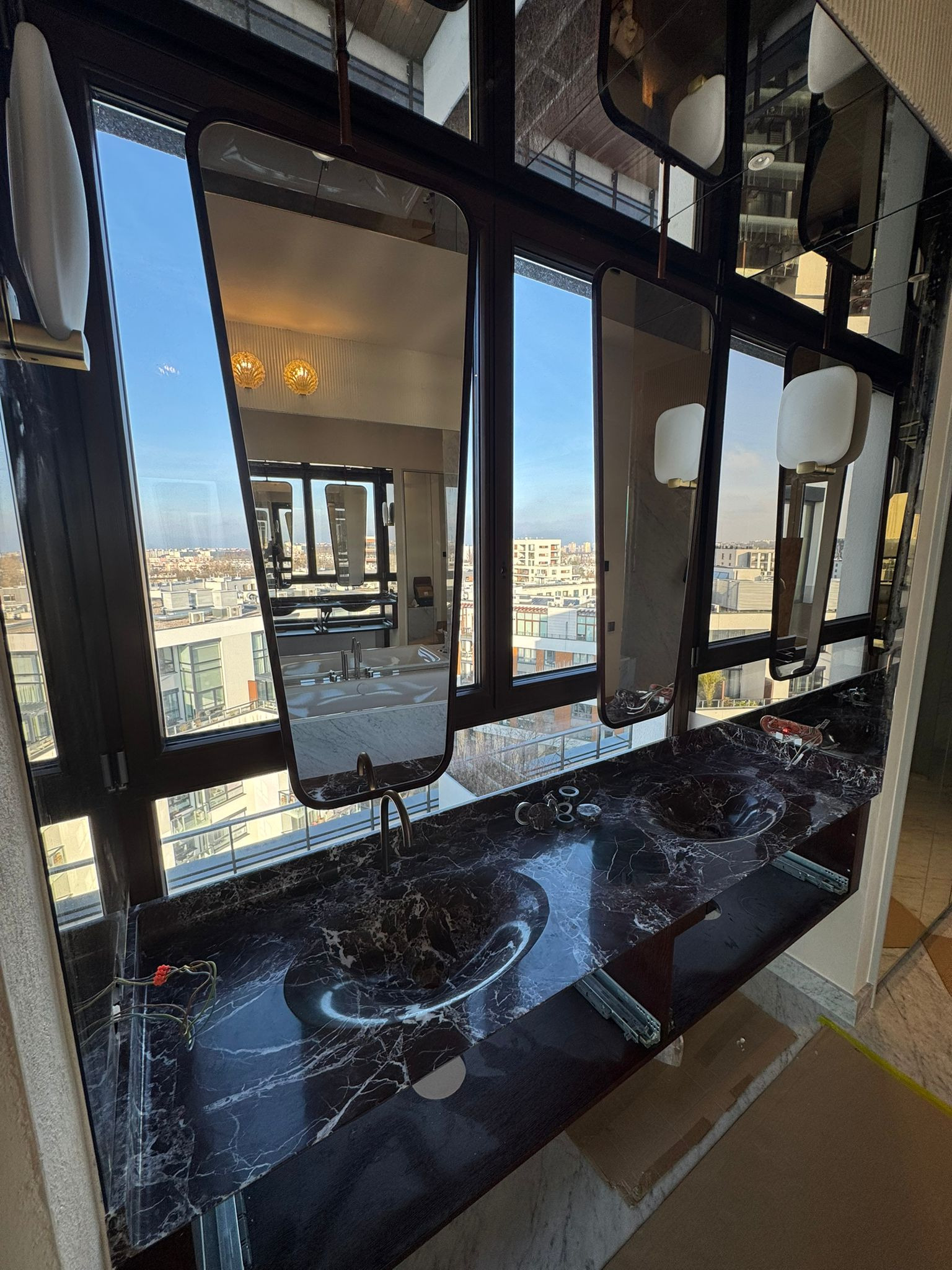 Ekskluzywna łazienka z czarnym marmurem, lustrami w ciemnych ramach i widokiem na miasto. Nowoczesny design z elementami luksusu i dbałością o detale.