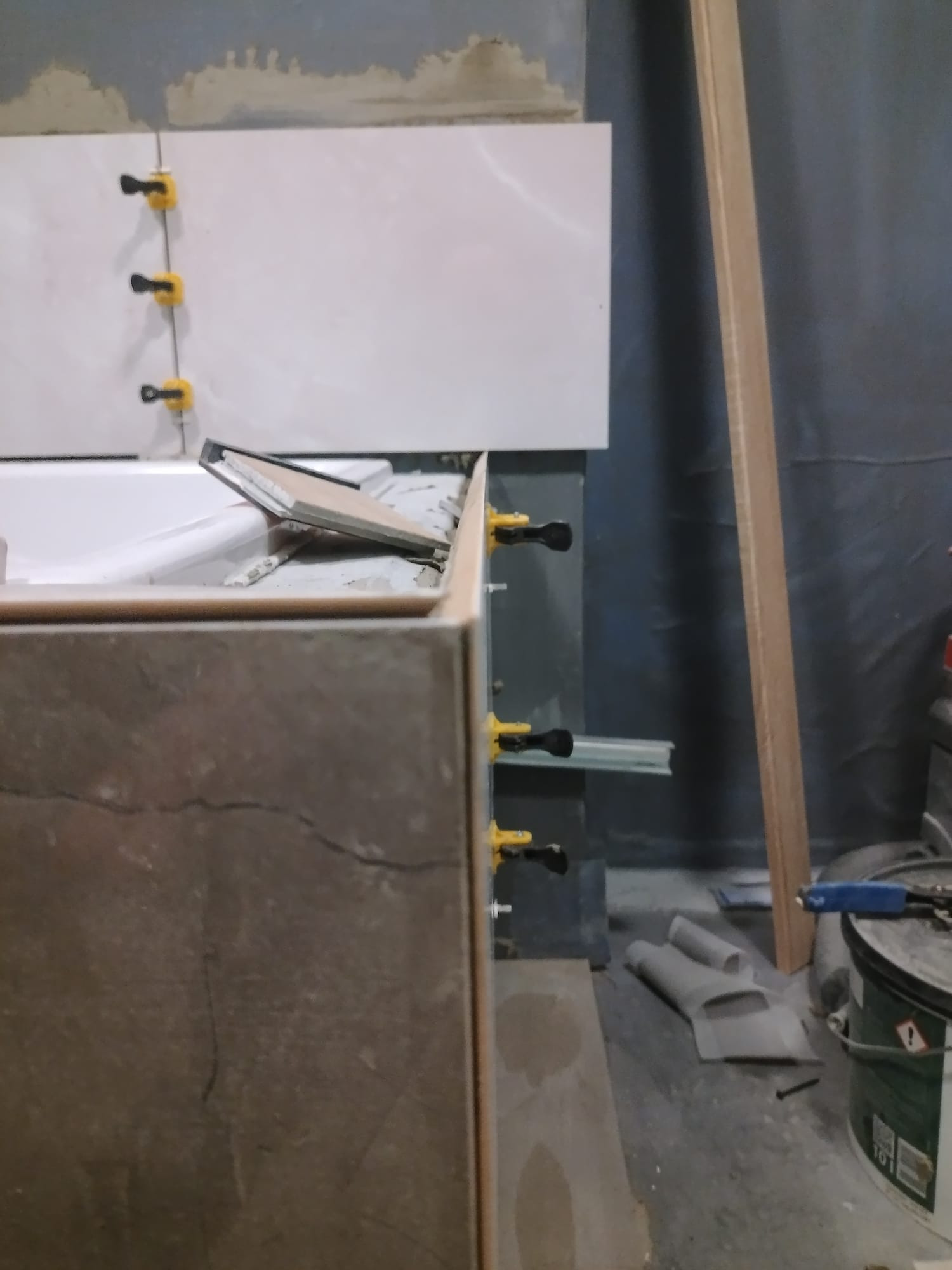 Montaż płytek w łazience z użyciem klipsów poziomujących. Widoczna wanna w zabudowie i narzędzia pracy. Ujęcie z bliska, podkreślające precyzję wykonania.