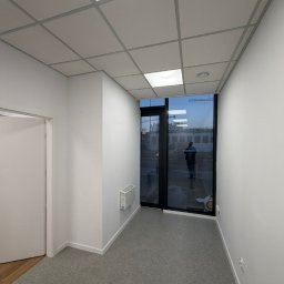 PK PIOSIMPLE SPÓŁKA Z OGRANICZONĄ ODPOWIEDZIALNOŚCIĄ - Wnętrze biura po remoncie w Orzesze: białe ściany, sufit podwieszany kasetonowy, szara podłoga, okno z widokiem na zewnątrz. Minimalistyczny design.