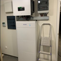 PanSolarnypl - Biała bateria i inwerter Sofar zamontowane na ścianie w pomieszczeniu, obok skrzynka elektryczna i drabina. Instalacja fotowoltaiczna wewnątrz budynku.