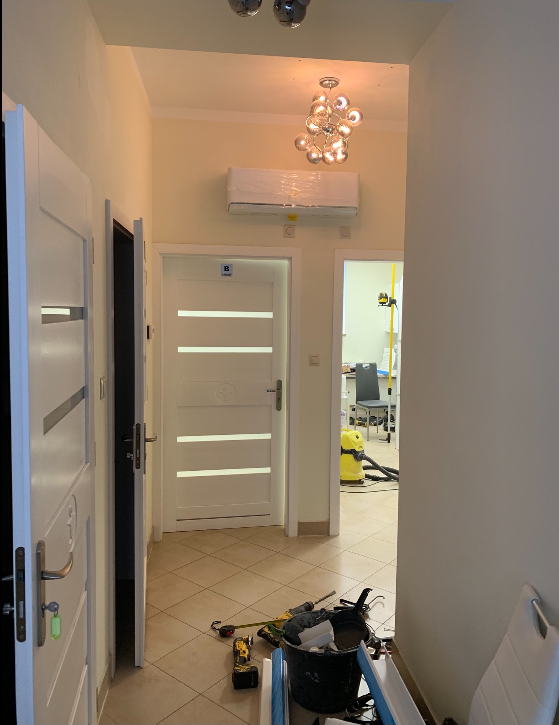 Korytarz po montażu klimatyzacji. Widoczny biały klimatyzator na ścianie, nowoczesna lampa sufitowa, drzwi z przeszkleniami i narzędzia na podłodze.