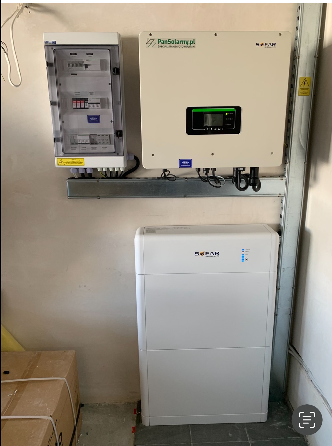 Biała bateria i inwerter fotowoltaiczny SOFAR zamontowane na ścianie, obok skrzynka z bezpiecznikami. Widoczne logo PanSolarny.pl.