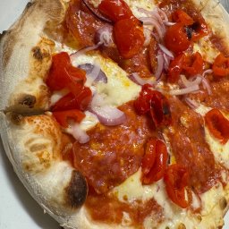MGD Marek Gałuszka - Neapolitańska pizza z salami, czerwoną cebulą i pieczoną papryką na cienkim cieście z lekko przypalonym brzegiem, serwowana na białym talerzu.