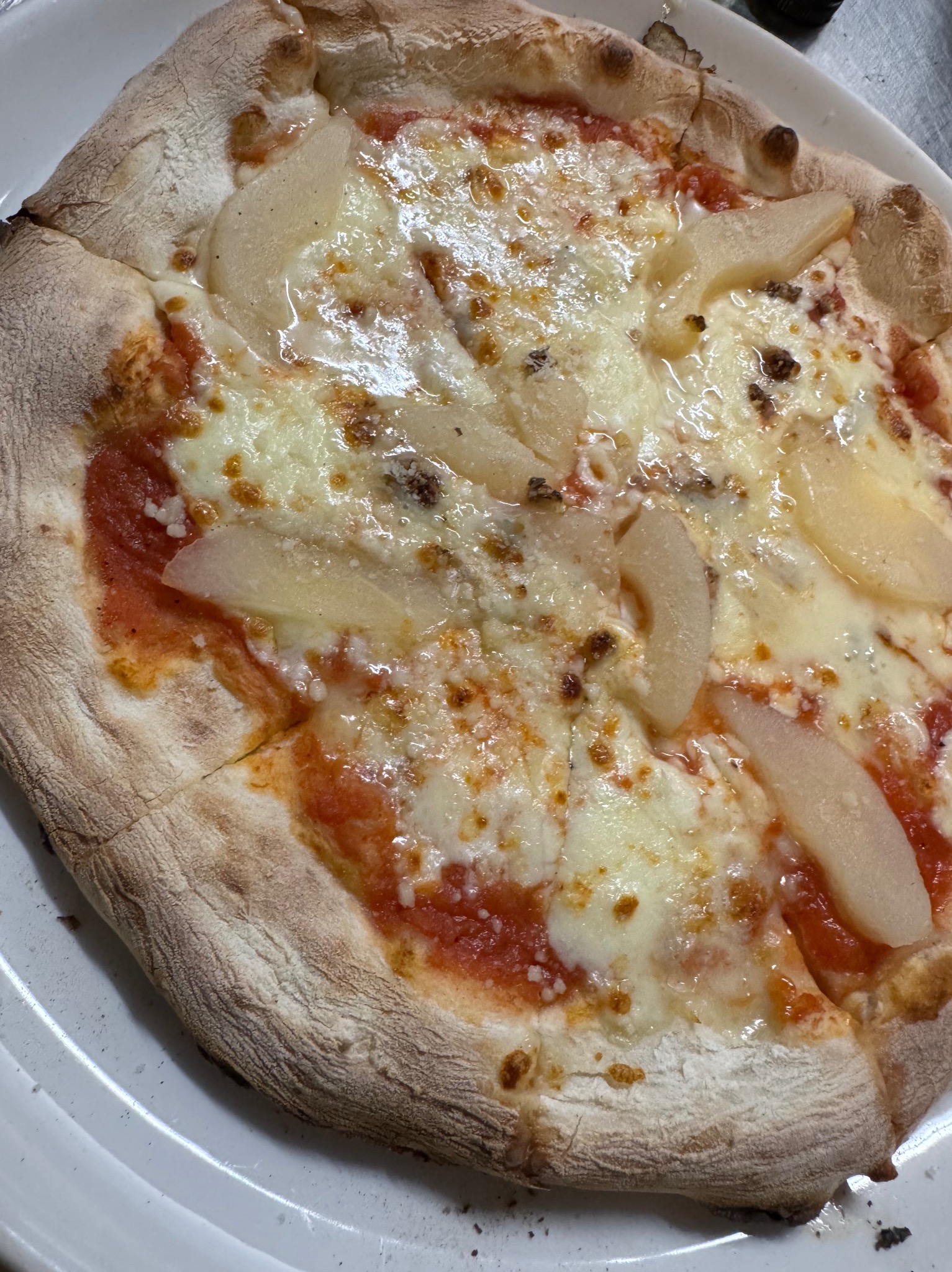 Pizza z gruszką i serem na cienkim cieście, widoczna na białym talerzu. Nietypowe połączenie smaków, bliski kadr, ostre światło.