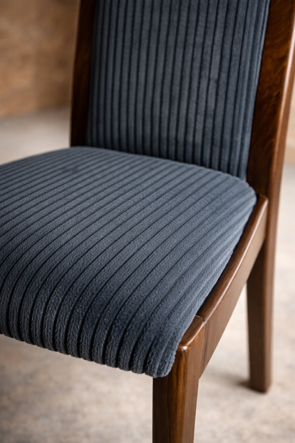 Detale tapicerowanego krzesła z ciemnoszarą, prążkowaną tkaniną i drewnianą ramą w ciepłym odcieniu brązu. Widoczne precyzyjne wykończenie i faktura materiału.