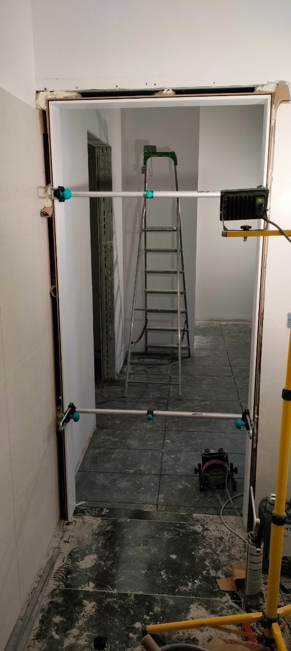 Montaż ościeżnicy w Gdyni. Widoczne narzędzia, drabina i fragmenty płytek podłogowych. Prace wykończeniowe w trakcie realizacji.