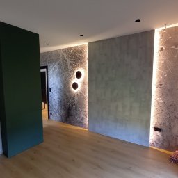 Sebastian Luty Firma remontowo wykończeniowa LUTERS - Nowoczesne wnętrze z szarą ścianą o fakturze betonu, zielonym filarem i podświetlaną ścianą z motywem drzewa. Parkiet na podłodze, czarne punkty świetlne na suficie.