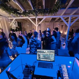Karol Giżewski Music & Events - DJ grający muzykę na imprezie pod zadaszeniem, widoczny sprzęt DJ-ski i tańczący ludzie w tle, oświetlenie w odcieniach niebieskiego.
