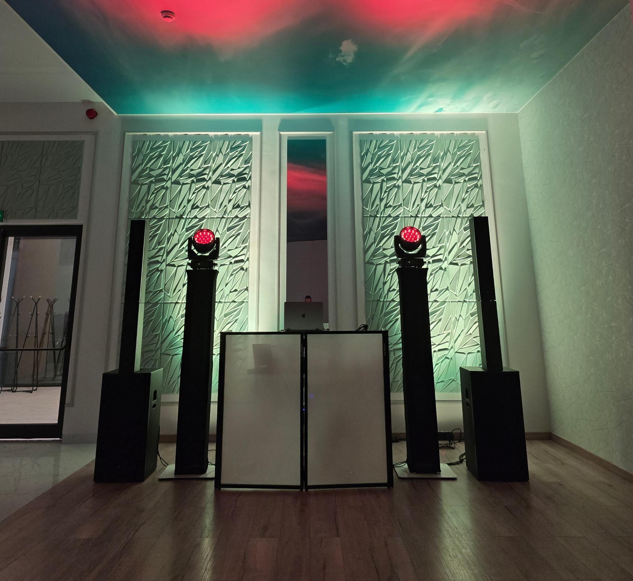 Rozstawiony sprzęt nagłośnieniowy i oświetleniowy z DJ-ką na tle dekoracyjnej ściany i sufitu z efektem nieba, gotowy do obsługi imprezy.