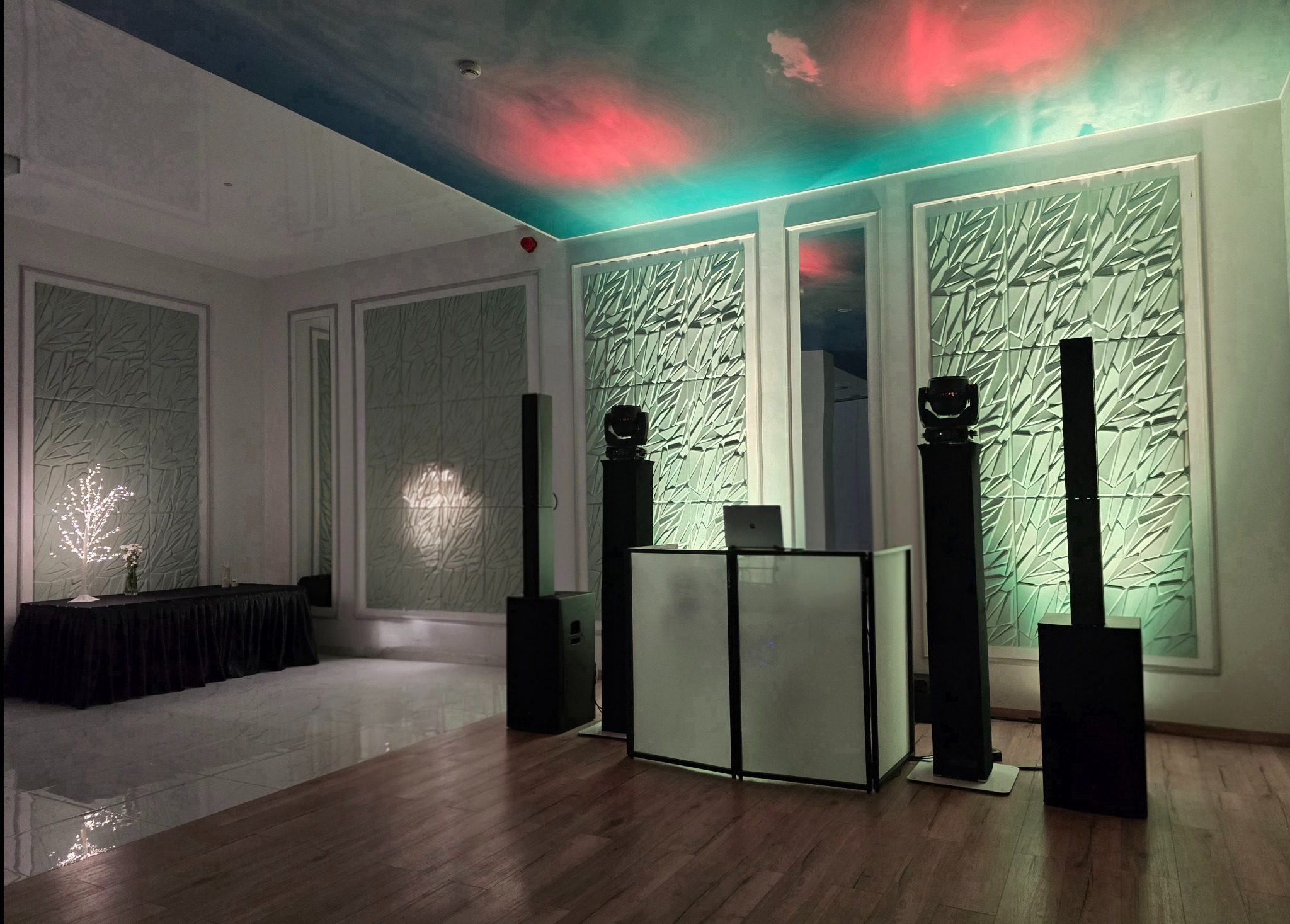 Sala bankietowa z nagłośnieniem i oświetleniem: kolumny głośnikowe, reflektory na statywach, stanowisko DJ-a z laptopem. Dekoracyjne panele ścienne i oświetlenie sufitowe.