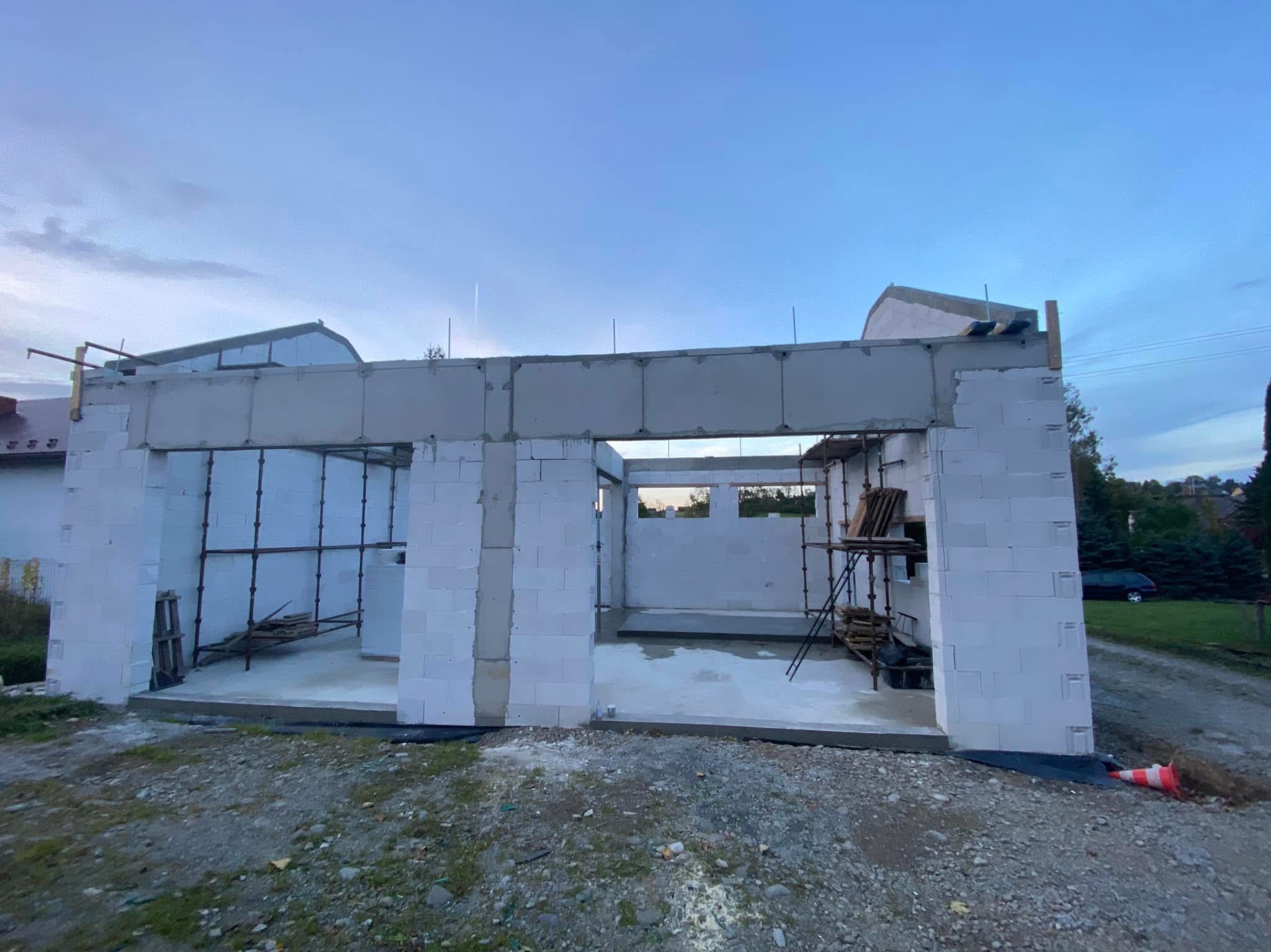Wznoszenie ścian parterowego domu z betonu komórkowego. Widoczne rusztowania i betonowy wieniec. Budowa w toku, stan surowy otwarty.