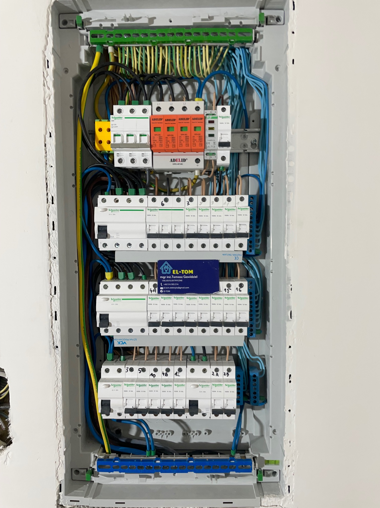 Rozdzielnica elektryczna w obudowie, widoczne zabezpieczenia, przewody i listwy zaciskowe. Na rozdzielnicy wizytówka firmy EL-TOM.