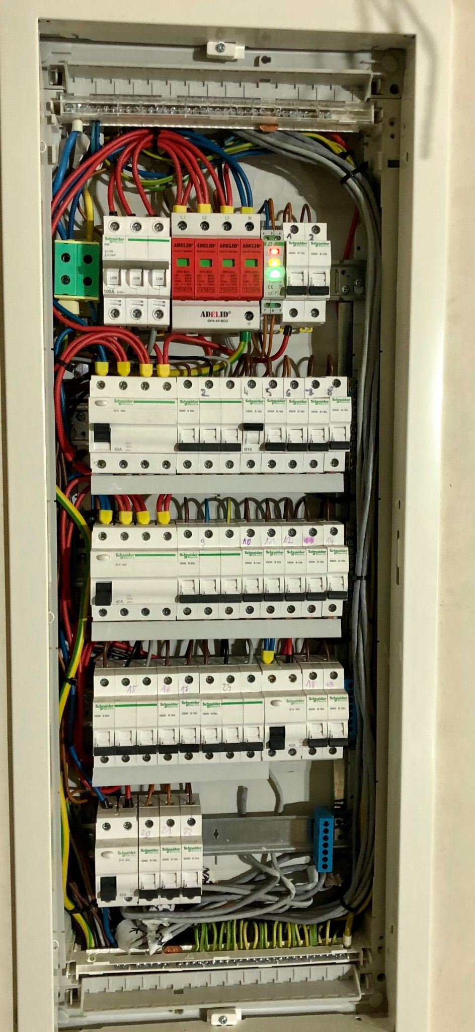 Rozdzielnica elektryczna z zainstalowanymi bezpiecznikami, przewodami i zabezpieczeniami przeciwprzepięciowymi marki Adelid, Schneider. Widoczne oznaczenia i numeracja.
