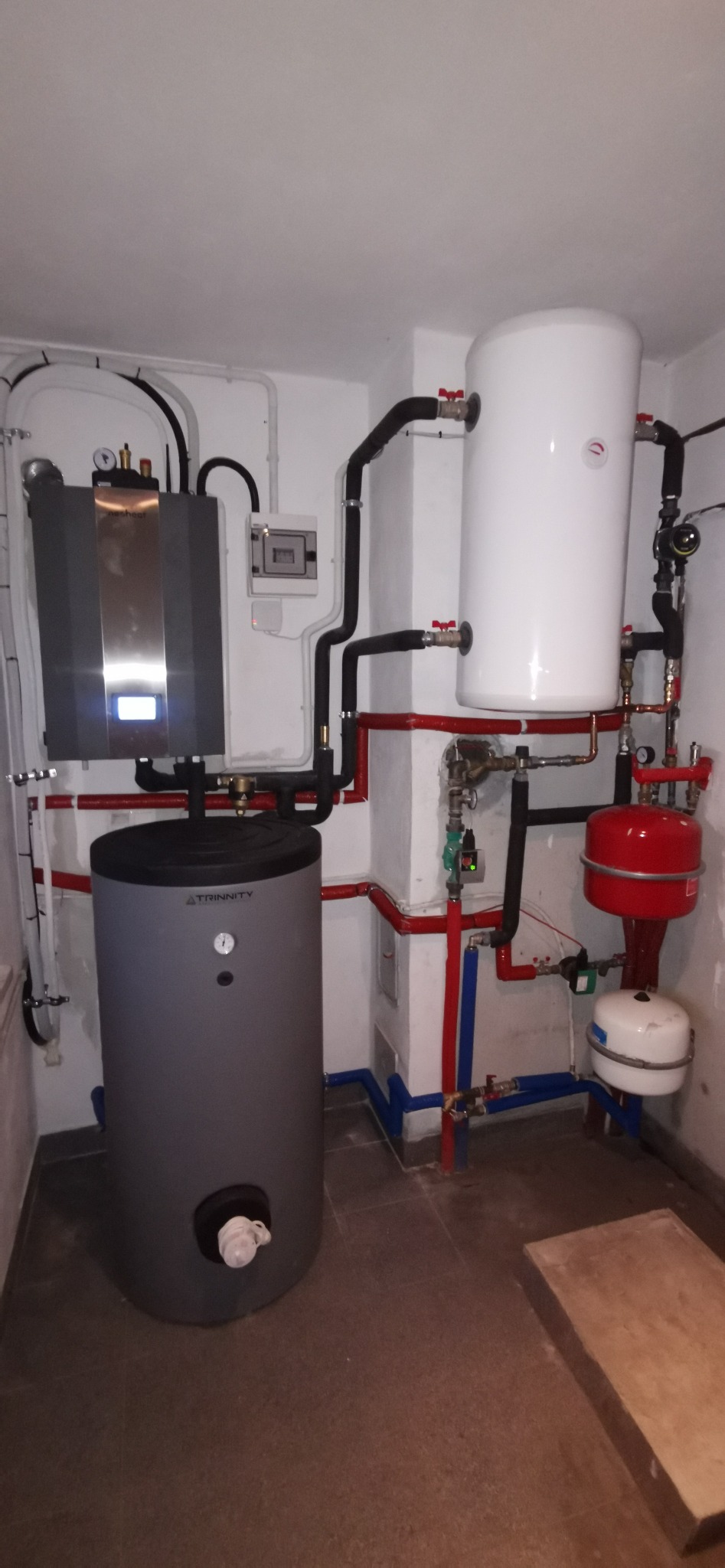 Zestaw kotła gazowego z zasobnikiem ciepłej wody w kotłowni, z widocznymi rurami instalacji grzewczej i elementami zabezpieczającymi.