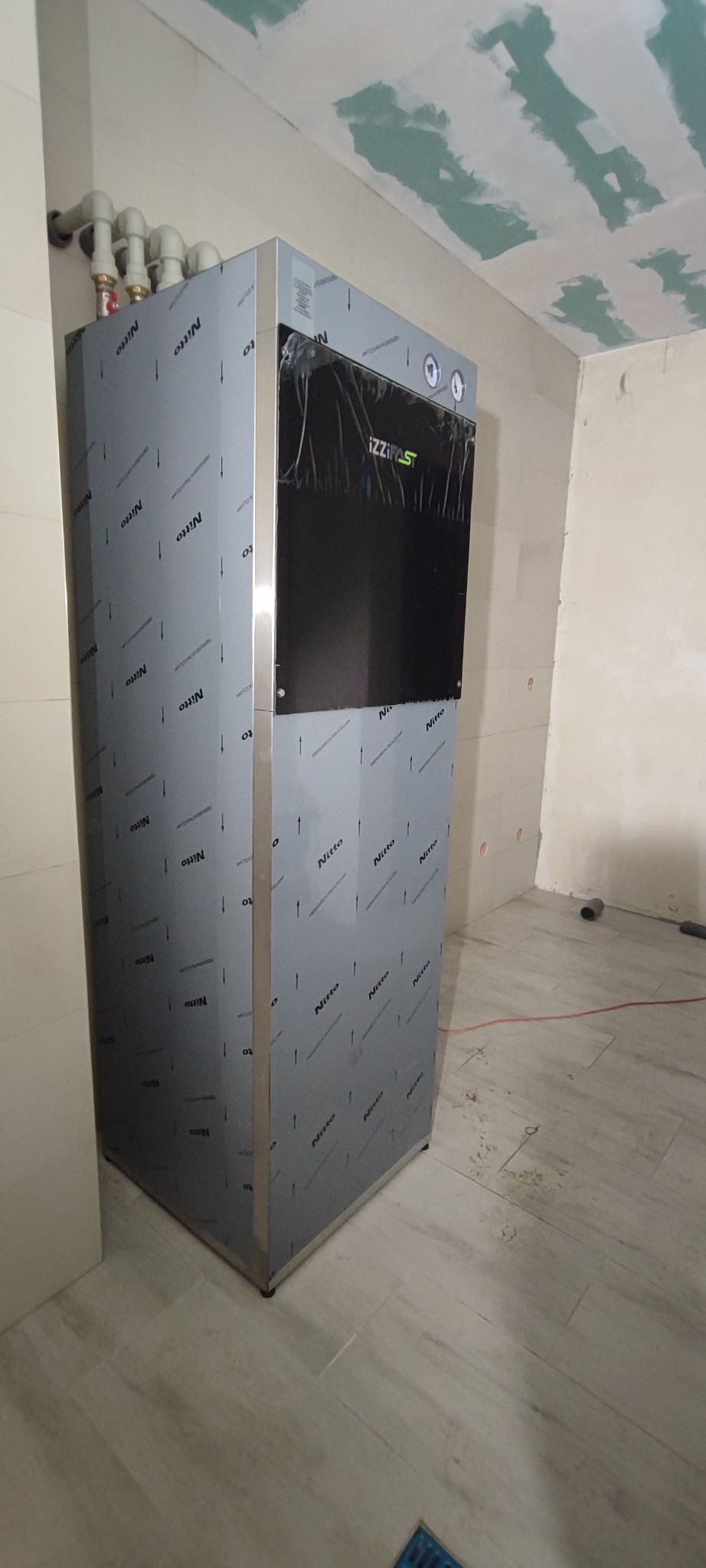 Nowoczesny piec gazowy IZZI FAST z podłączeniem rur w pomieszczeniu w trakcie wykończenia, widoczne płyty gipsowe na suficie.