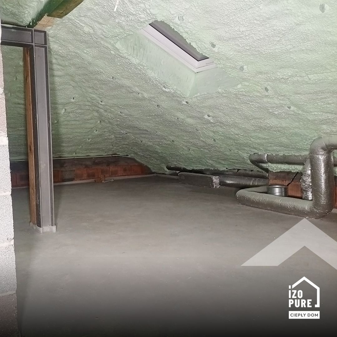 Poddasze po aplikacji pianki izolacyjnej, widoczne okno dachowe i rury wentylacyjne. Jasnozielona, nierówna powierzchnia pianki pokrywa skośny dach.