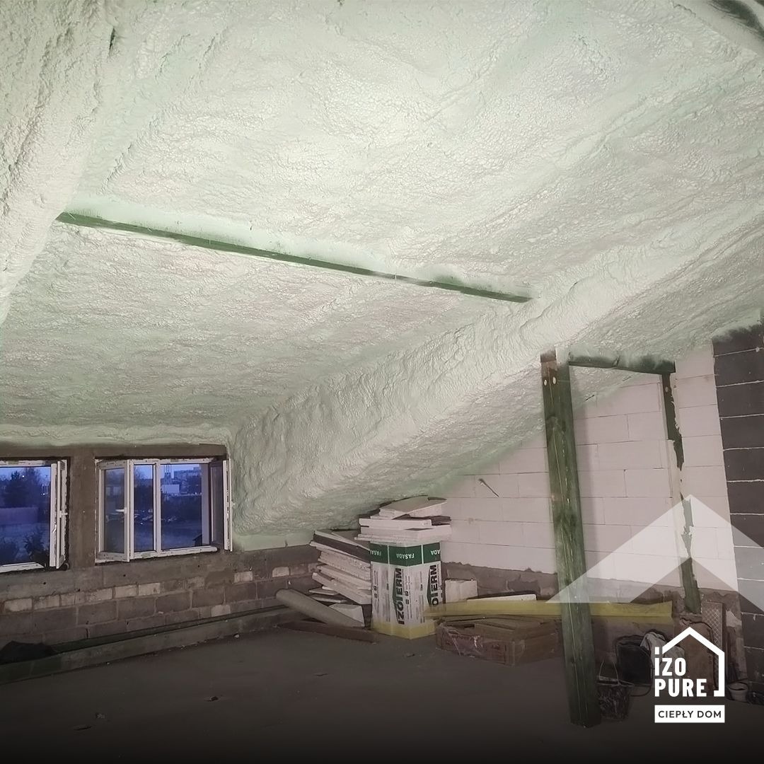 Poddasze po natrysku pianki PUR, widoczne okna dachowe i skosy. Na podłodze leżą płyty izolacyjne. Widoczna faktura pianki na suficie i ścianach.